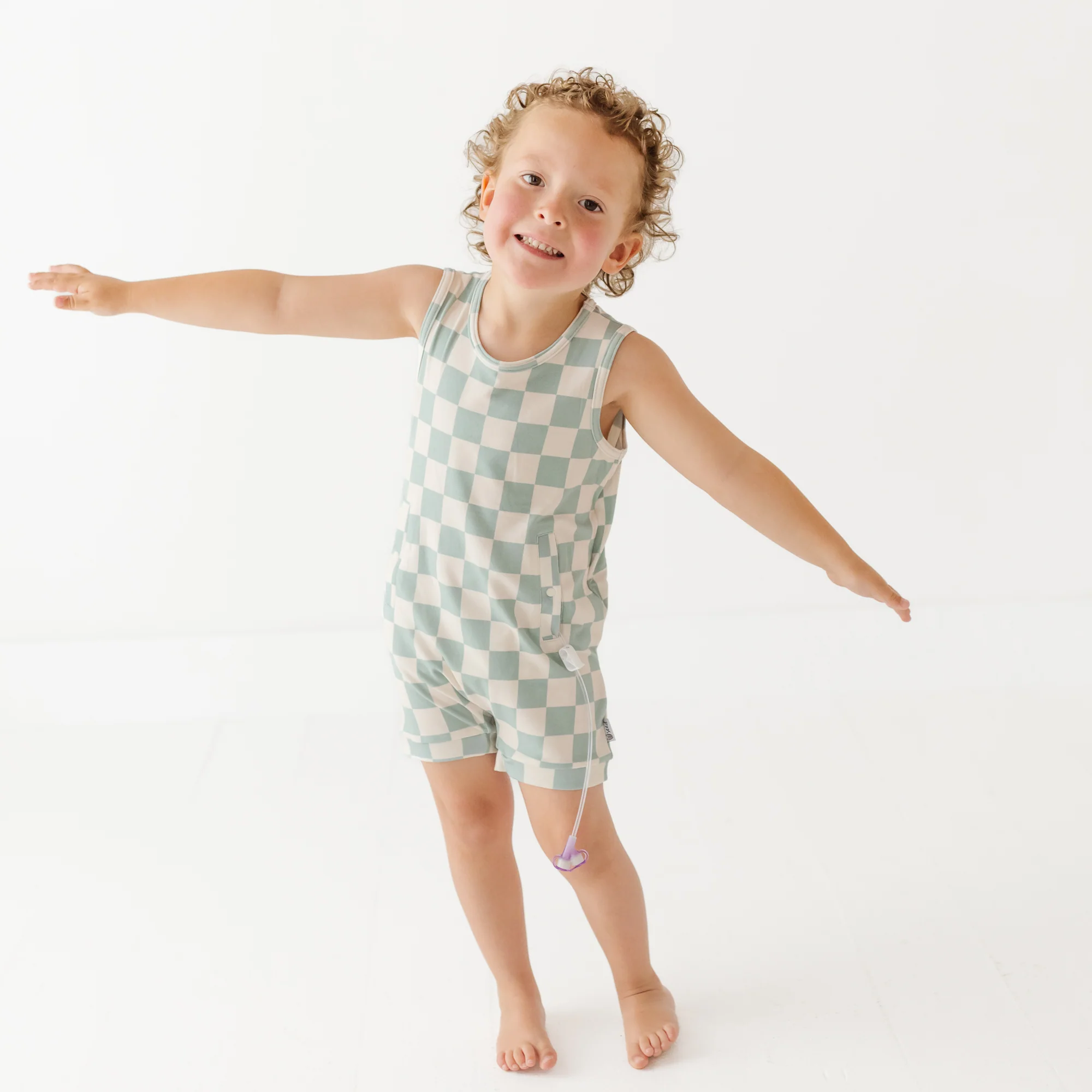 Boy impersonates an aeroplane in checked romper